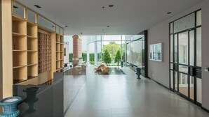 Un vestíbulo amplio con diseño moderno, que incluye un mostrador de recepción, un gran ventanal y una zona de estar con una fuente de agua.