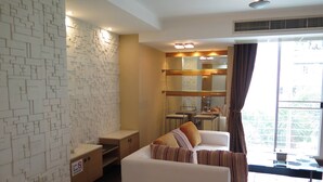 A modern living room with a white sofa, a patterned wall, and a dining area visible through a glass partition. - 4B - 2 Bedroom Downtown Apartment With Shared Pool (Bangkok)