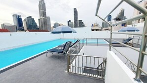 A rooftop pool with lounge chairs and umbrellas, surrounded by city skyscrapers. - 4B - 2 Bedroom Downtown Apartment With Shared Pool (Bangkok)