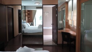 A hotel room with a bed, a desk, and a chair. There is a door leading to another room. - 4B - 2 Bedroom Downtown Apartment With Shared Pool (Bangkok)