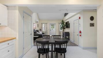 A compact kitchen with a dining area, white tiled flooring, and a view into a living room with a sofa and curtains.