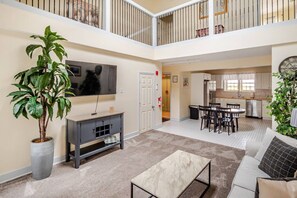 A spacious living area with a flat-screen TV, a dining table with chairs, a sofa, and a potted plant.
