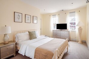 A hotel room with a bed, bedside tables, a TV, and a window with curtains.