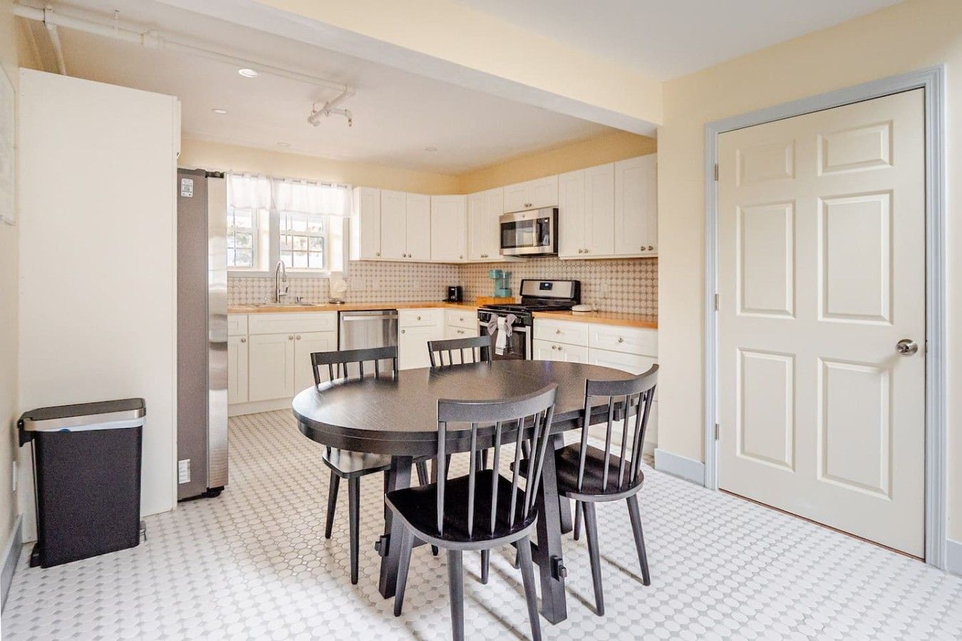A compact kitchen with white cabinets, a microwave, and a dining table with chairs.