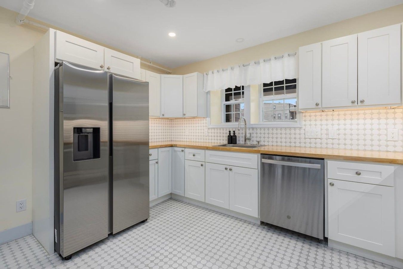 A kitchen with white cabinets, a stainless steel refrigerator, a dishwasher, and a tiled backsplash.