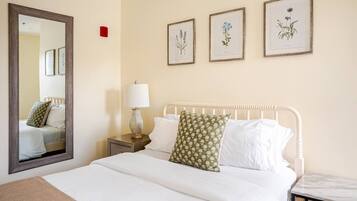 A hotel room with a bed, a nightstand, a lamp, a mirror, and three framed botanical prints on the wall.