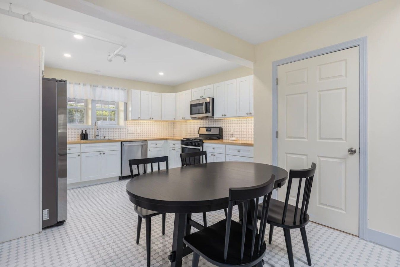 A modern kitchen with white cabinets, a microwave, and a dining area with a round table and chairs.