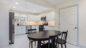 A modern kitchen with white cabinets, a microwave, and a dining area with a round table and chairs.