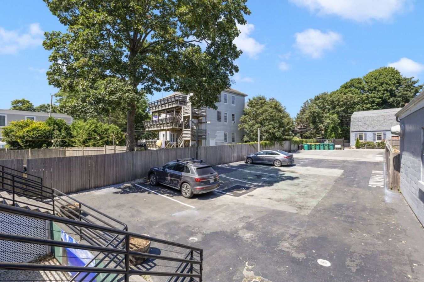 Un espace de stationnement avec deux voitures, un bâtiment doté d’un balcon et un arbre en arrière-plan.