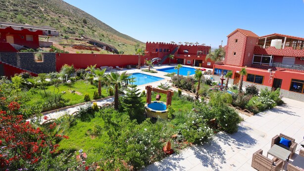 A resort with a swimming pool, lush garden, and red buildings. - Hotel palais d'orient (Tafoughalt)