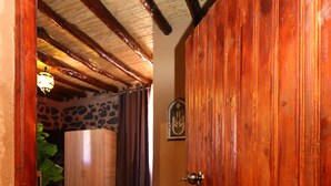 A wooden door leading to a bedroom with a bed, a wardrobe, and a stone wall. - Hotel palais d'orient (Tafoughalt)