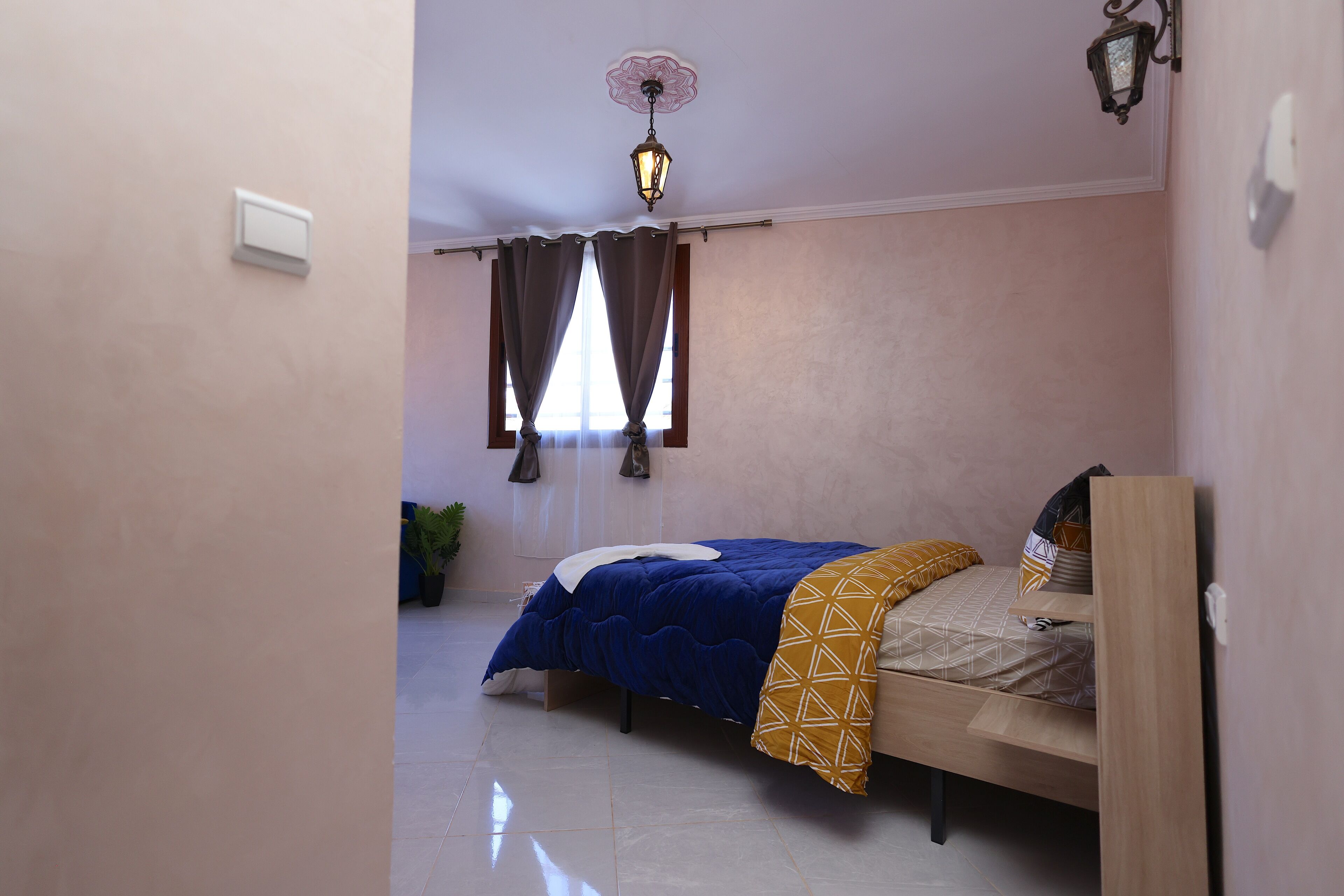 A small bedroom with a single bed, a ceiling light, and a window with curtains.