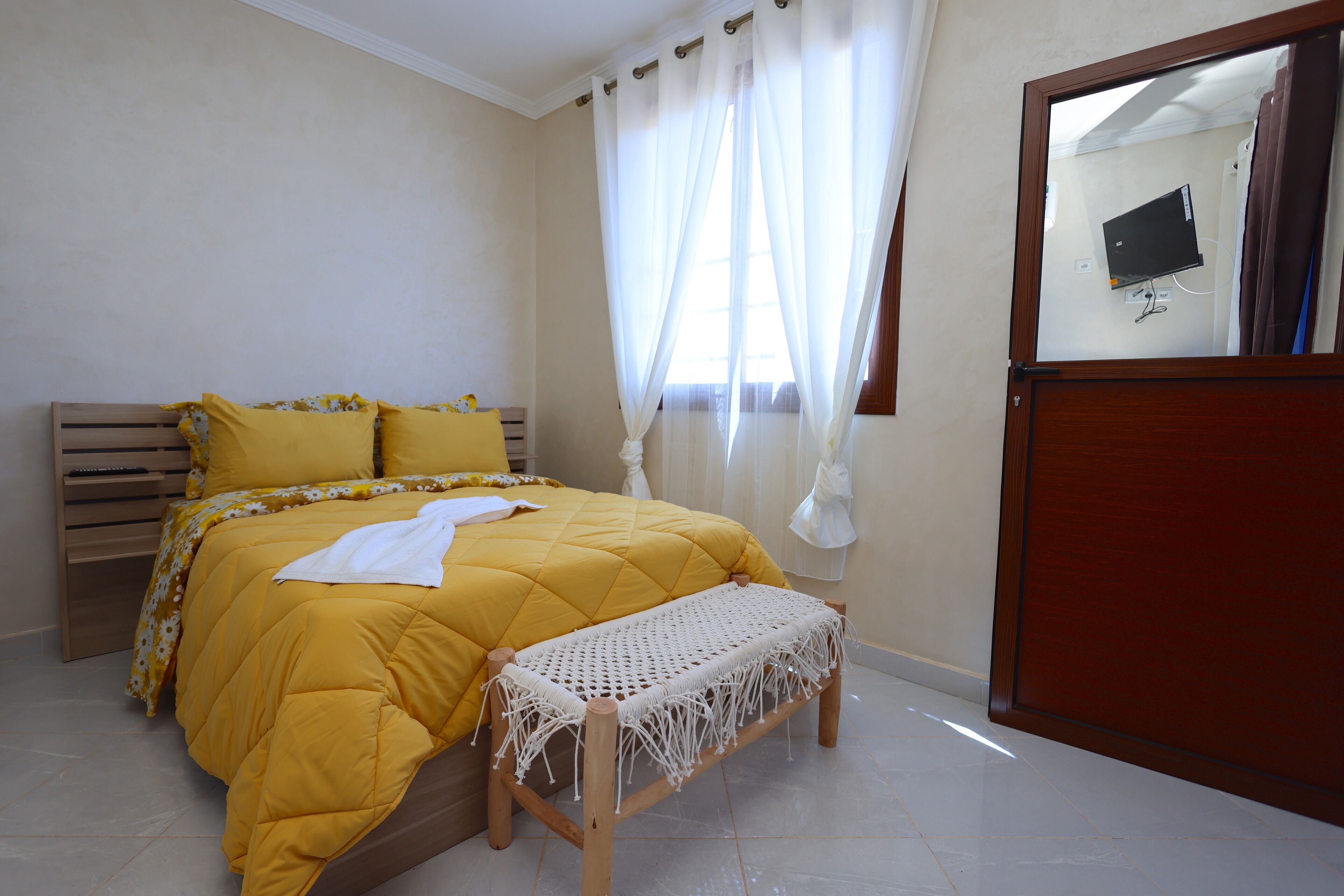 Un dormitorio con cama, banca, espejo y cortinas.