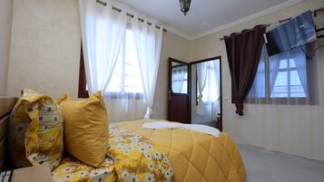 A bedroom with a bed, curtains, a television, and a door.