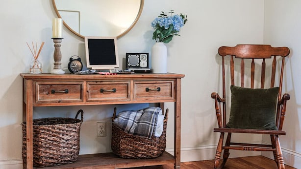 Een houten bureau met lades, een ronde spiegel, een oude radio en een vaas met blauwe bloemen.