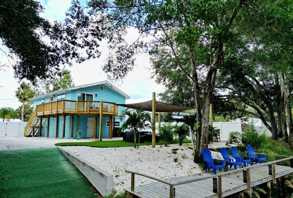 A beachfront property with a blue building, a wooden deck, and blue chairs.