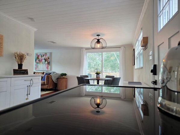 A modern kitchen with white cabinetry, a dining area with a round table, and a large window offering a view of greenery.