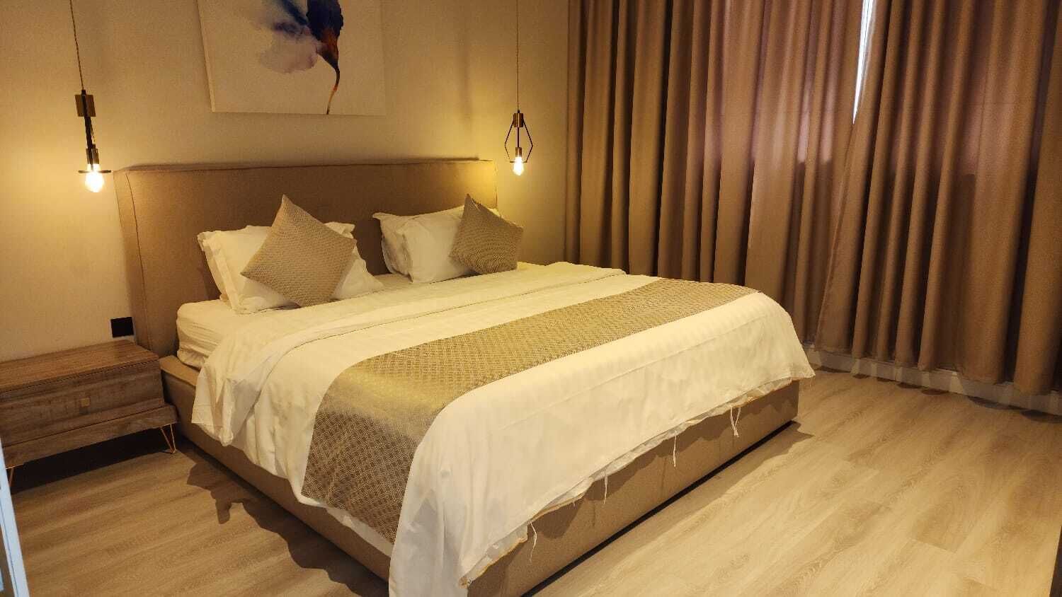 A neatly made bed with a white and beige bedspread, two bedside lamps, and a wooden nightstand.