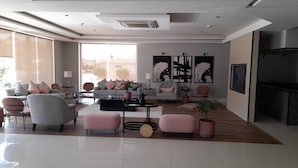 A spacious living room with a grey sofa, pink ottomans, and a coffee table. There are three large abstract paintings on the wall and a fireplace on the right. - ALWURUD ALARBA FOR SERVICED APARTMENTS (Riyadh)