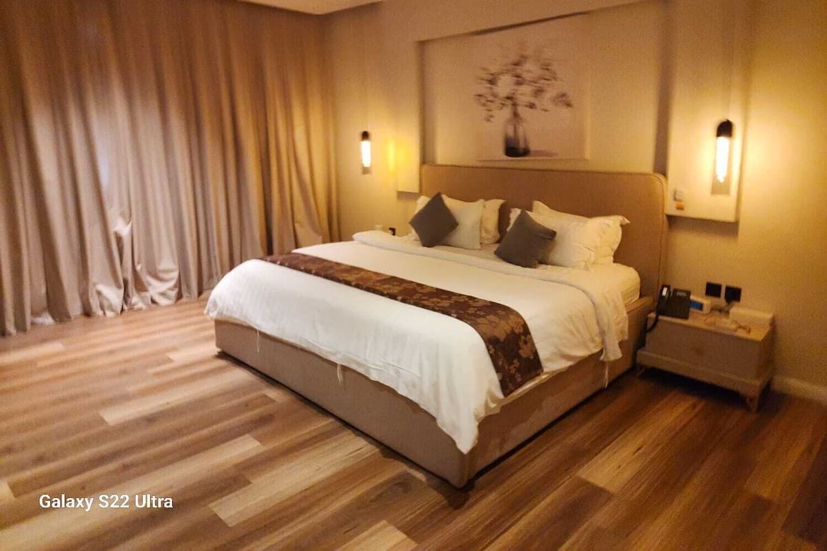 Une chambre spacieuse avec un grand lit, un plancher en bois et une table de chevet avec une lampe.