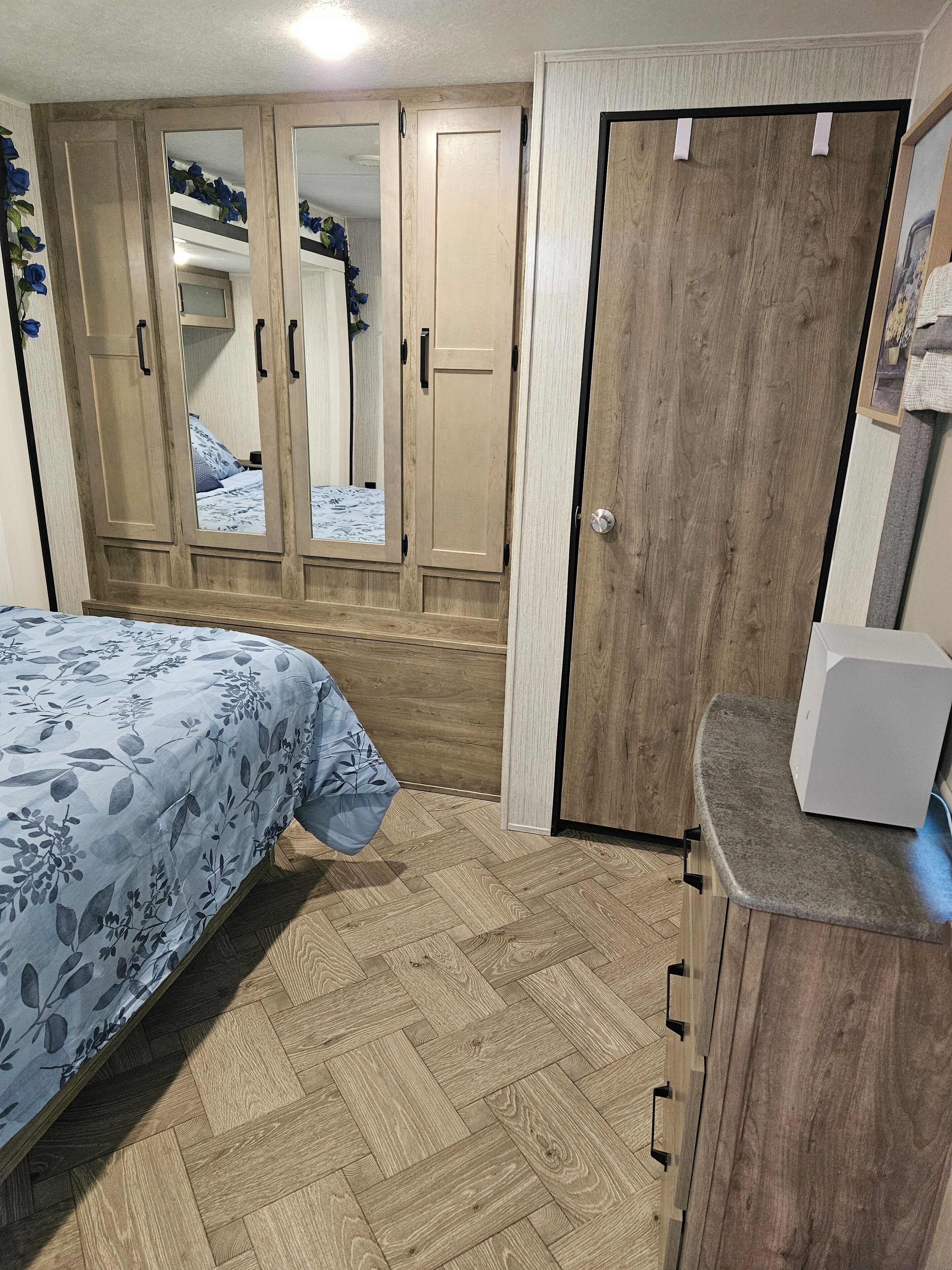 Ein Schlafzimmer mit einem Bett, einem Kleiderschrank, einem Spiegel und einer kleinen Küchenzeile.