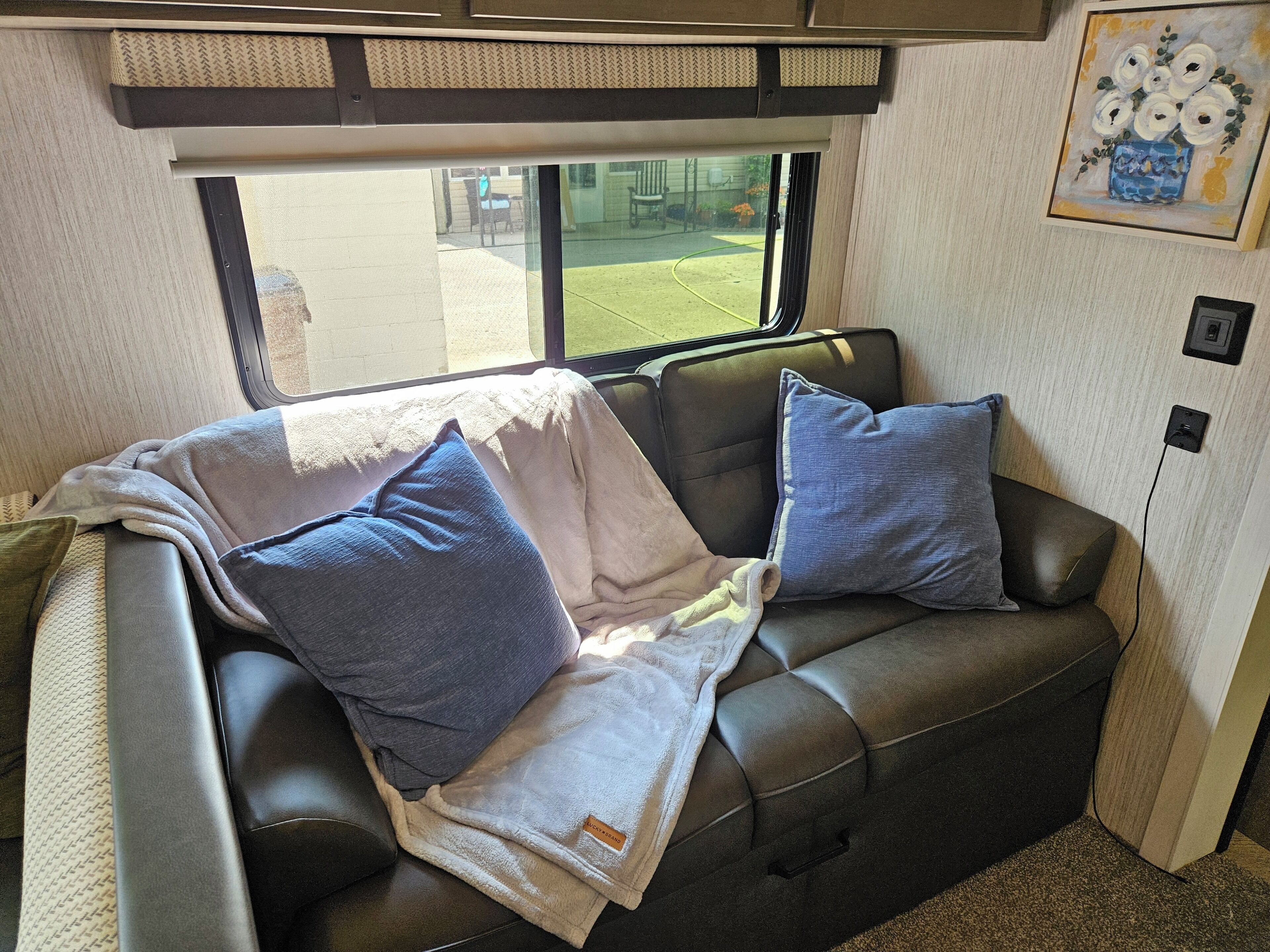 A cozy interior with a leather couch, two pillows, a blanket, and a window offering a view of the outdoors.