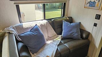 A cozy interior with a leather couch, two pillows, a blanket, and a window offering a view of the outdoors.