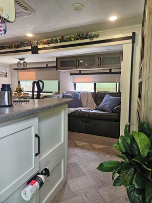 Un intérieur de camping-car compact comprenant un coin cuisine, un espace salon et une fenêtre offrant une vue.