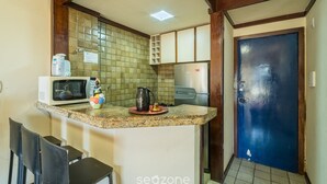 A kitchen with a microwave, a kettle, and a coffee maker on the counter. There are two chairs and a blue door in the background. - Apartment With Balcony and sea View - Ier0305 (Salvador)