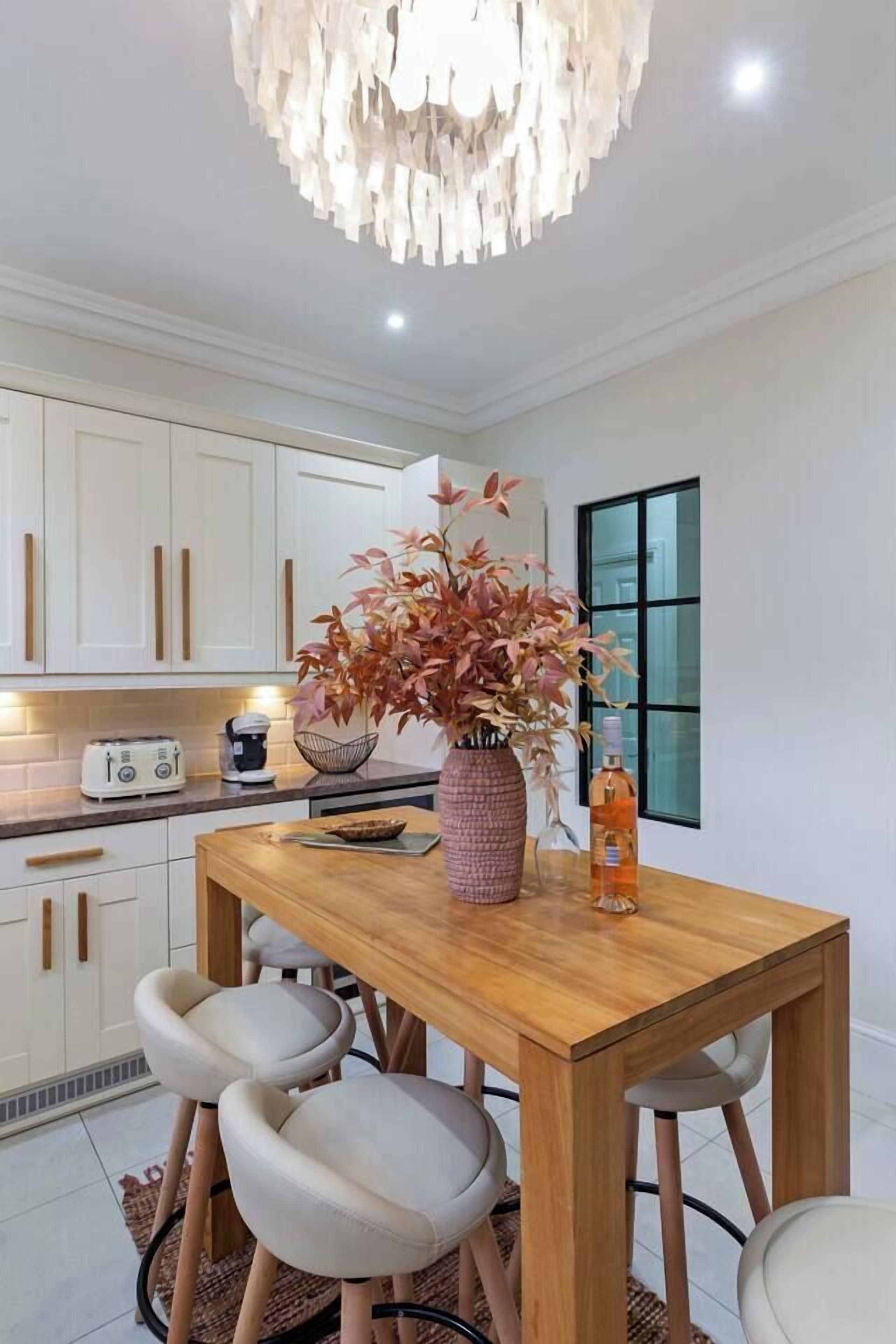 Una cocina moderna con armarios blancos, una mesa de comedor de madera y una lámpara de techo original.