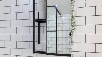 Un bagno con un lavandino bianco, un rubinetto nero e uno specchio con cornice nera. Sono presenti due flaconi di sapone e un rotolo di carta igienica a parete.