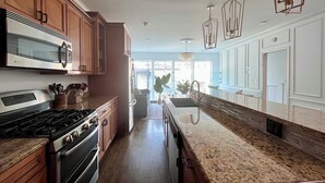 A modern kitchen with wooden cabinets, stainless steel appliances, granite countertops, and pendant lighting. - 6 BDRM/ 6 BATH LUX Avondale Home, Sleeps 15, Rooftop Deck & 2 Car Garage! (Chicago)
