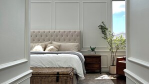A bedroom with a large bed, a chest of drawers, a potted plant, and a view of the sky through a window. - 6 BDRM/ 6 BATH LUX Avondale Home, Sleeps 15, Rooftop Deck & 2 Car Garage! (Chicago)