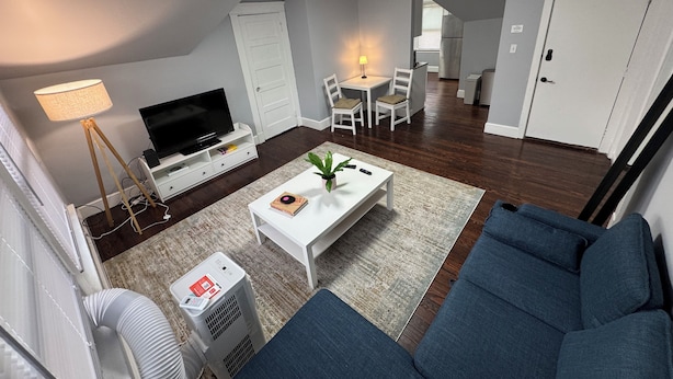 A modern living room with a sofa, a coffee table, a TV, and a dining area with chairs. - Spacious Yale 2BR with Full Kitchen & WiFi (New Haven)