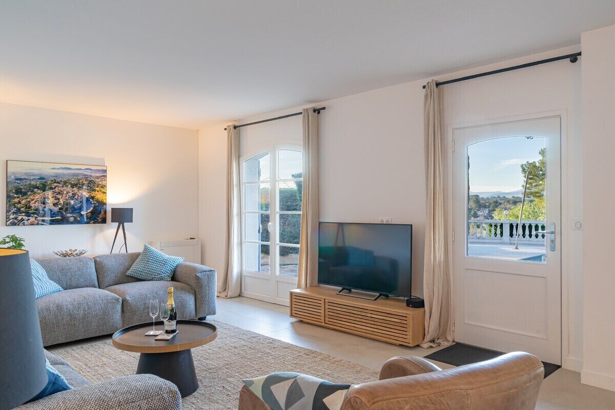 A modern living room with a sofa, a coffee table, a TV, and a balcony with curtains.