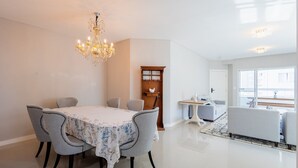 Et moderne spiseområde med en lysekrone, et spisebord med blomstret dug og grå polstrede stole.