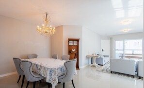 A modern dining area with a chandelier, a dining table with floral tablecloth, and grey upholstered chairs. - Apart With Barbecue 550m From the Beach Raa0301 (Itapema)