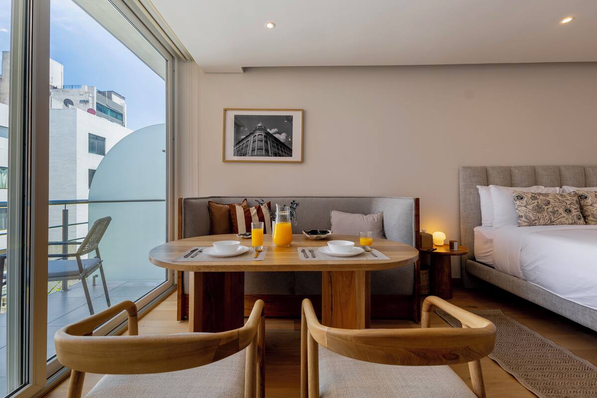 Una habitación de hotel moderna con zona de comedor, cama y vistas a la ciudad.