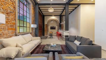 Un salon moderne avec un mur en briques, une grande fenêtre et une cheminée. On y trouve deux canapés, une table basse et un coin repas avec des chaises rouges.