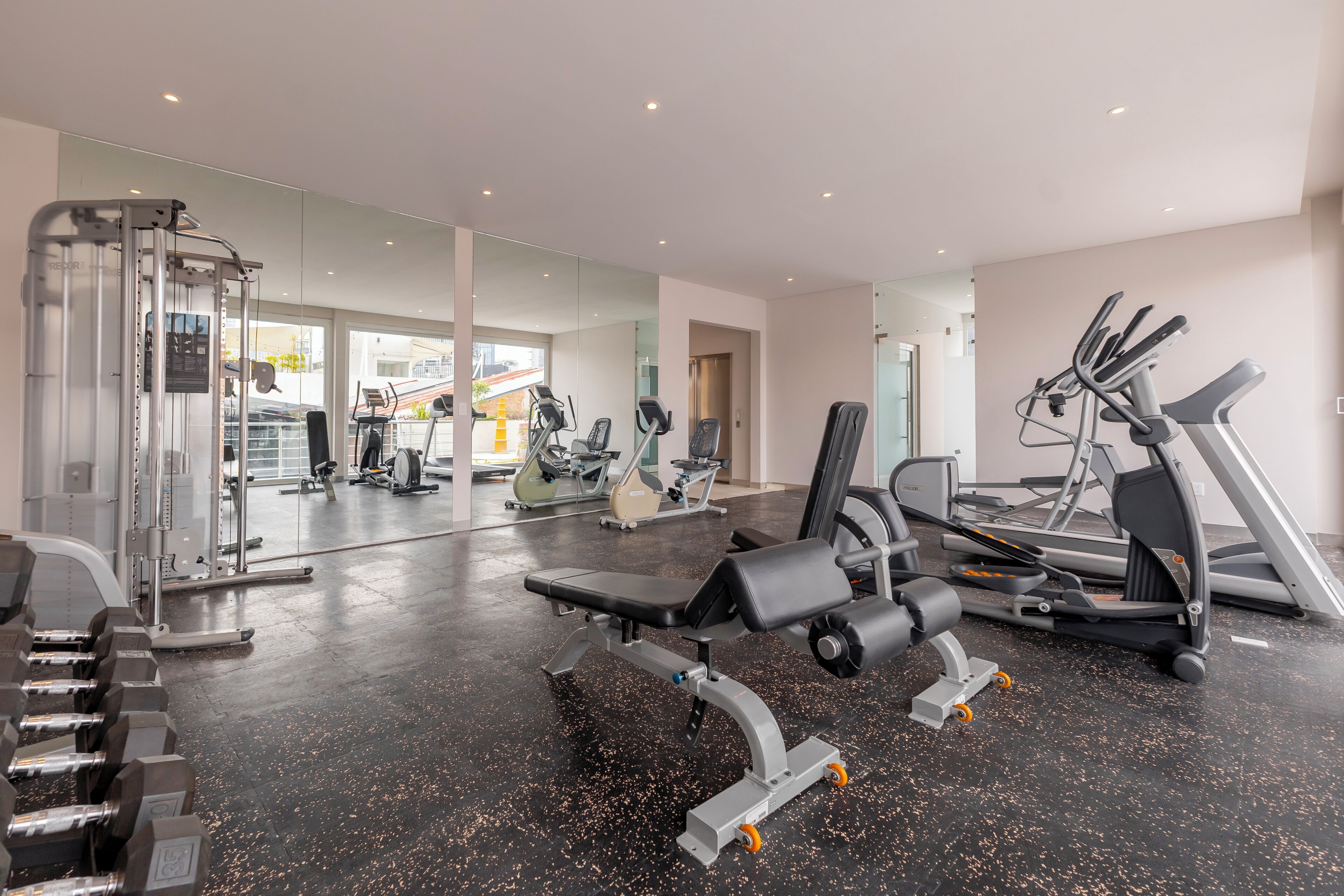 A gym with exercise equipment, a bench, and a mirrored wall.
