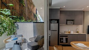 Une cuisine moderne dotée d’appareils électroménagers intégrés, un coin repas avec une table et des chaises, et une vue sur un mur de roche naturelle.
