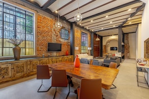 A spacious room with a large wooden table, multiple chairs, a television, and a brick wall.