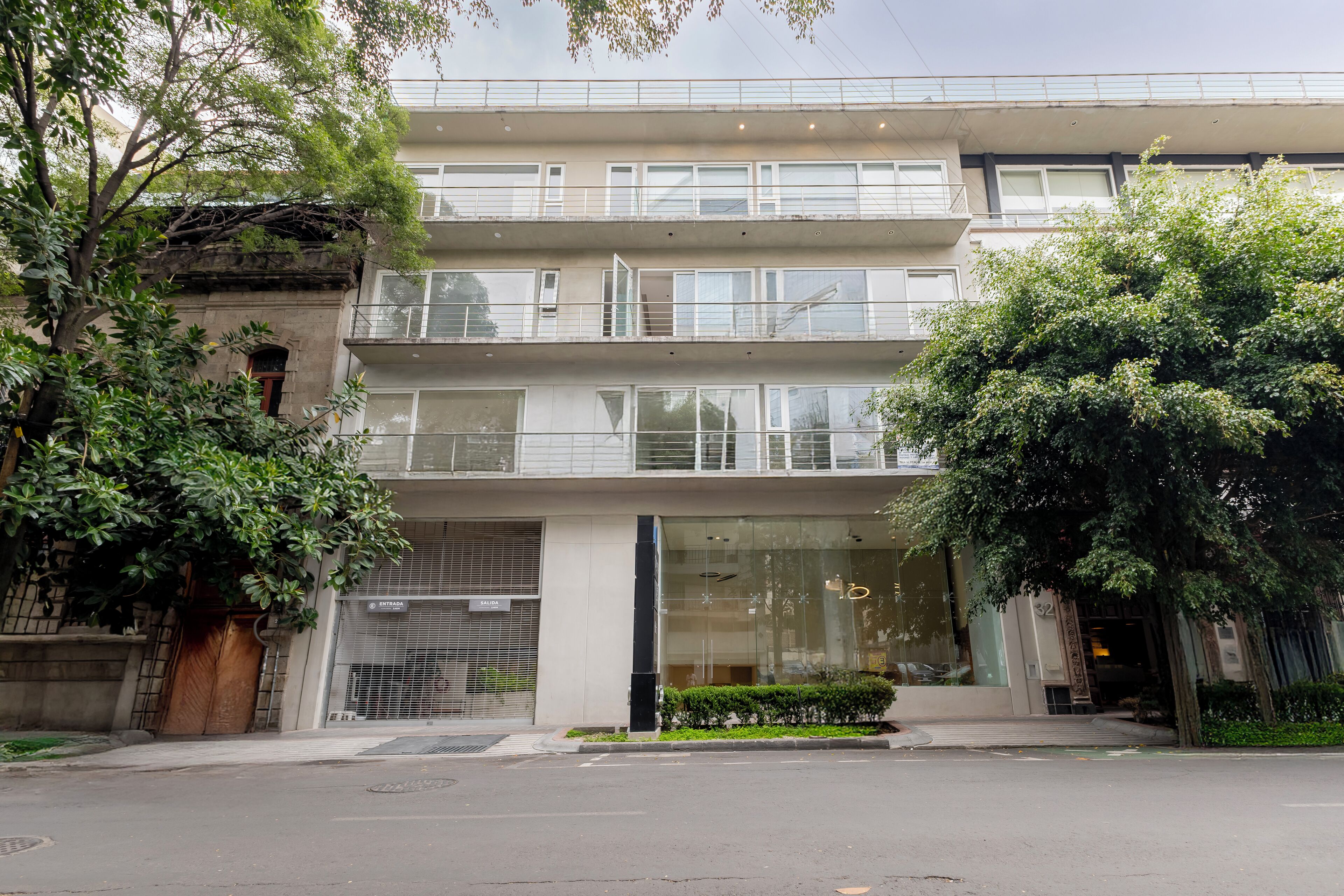 Edifício de vários andares com design arquitetônico moderno, com varandas nos andares superiores e uma grande entrada de vidro.
