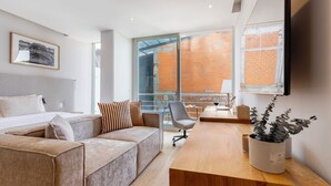 Une chambre d’hôtel moderne, dotée d’un grand lit, d’un canapé, d’un bureau en bois et d’une grande fenêtre donnant sur un immeuble en briques.