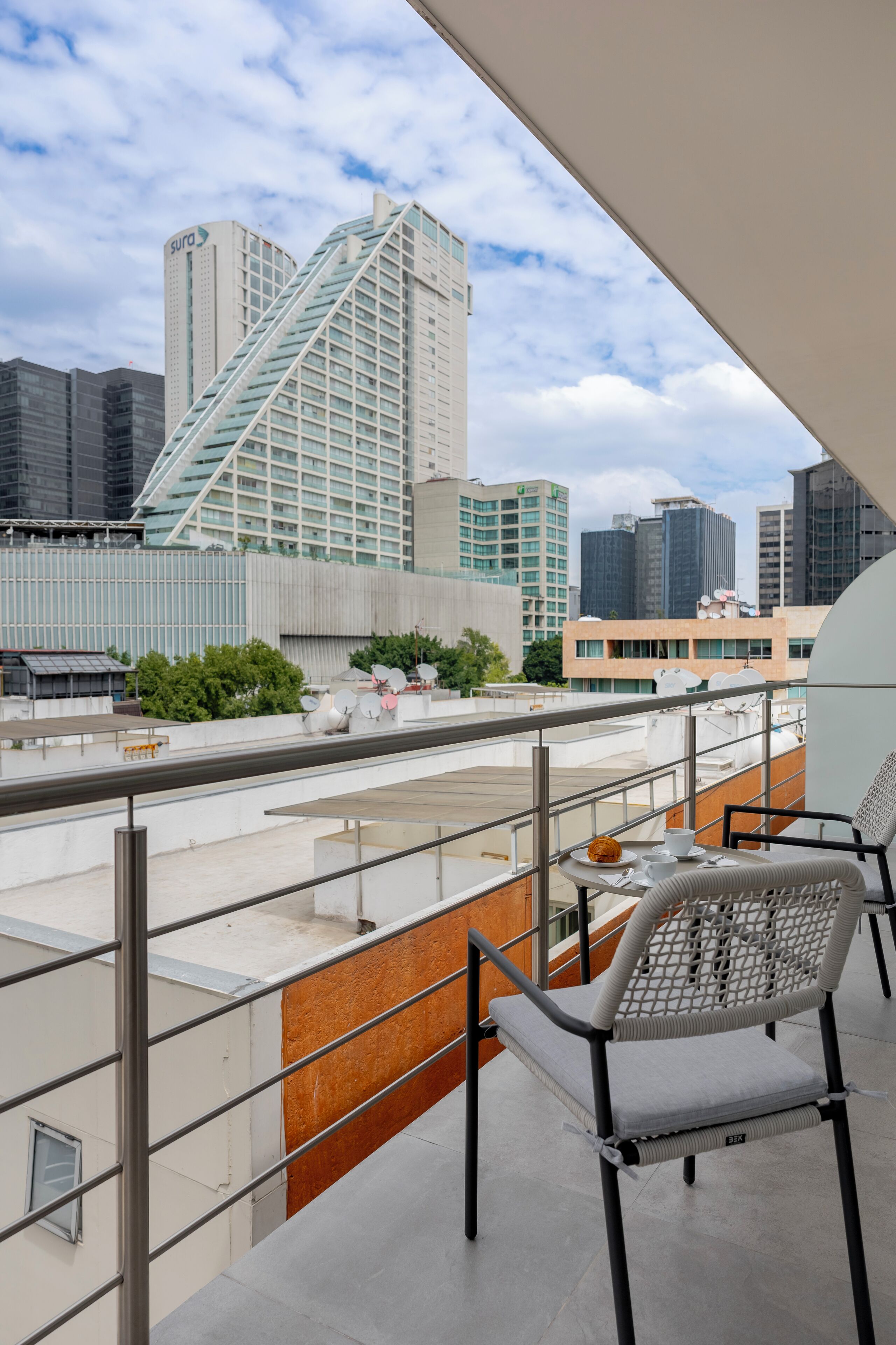 Ein Balkon mit Blick auf eine Stadtlandschaft, darunter moderne Gebäude und ein markanter Turm.