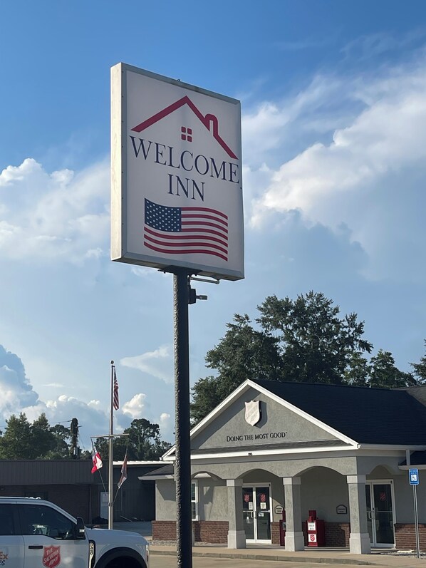 Letrero de Welcome Inn con una bandera estadounidense, un edificio de Cruz Roja en el fondo y un cielo despejado.