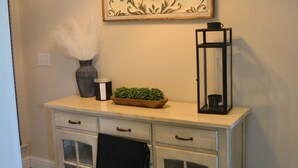 Un couloir avec une console blanche, un vase décoratif, une petite plante, une lanterne noire et un tapis à motifs.