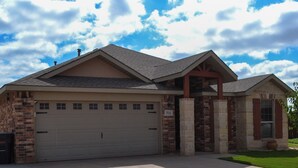 Une maison à deux étages avec un garage, une façade en pierre et une pelouse bien entretenue.