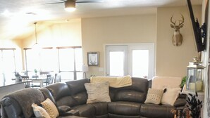 Un salon moderne avec un canapé d’angle, un ventilateur de plafond et une tête de cerf fixée au mur.