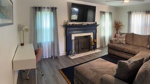 Ein Wohnzimmer mit Kamin, einem darüber montierten Fernseher, einem Deckenventilator und einem Sofa.